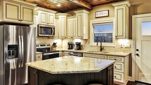A kitchen with a stainless steel refrigerator, a microwave, a coffee maker, and a large island with bar stools.
