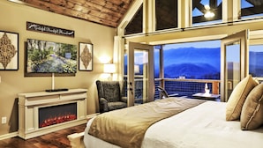 A spacious bedroom with a fireplace, a large bed, a television, and a balcony with a mountain view.