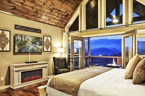 Ein geräumiges Schlafzimmer mit Kamin, einem großen Bett, einem Fernseher und einem Balkon mit Bergblick.