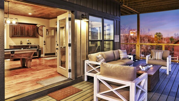 An outdoor deck with white furniture, a pool table, and a fire pit.