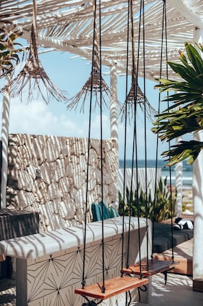 A beachside lounge with a stone wall, hanging light fixtures, and a cushioned seating area. - Casa Xuul Oceanfront Villa • Chef • Staff, Pools, Hot tub & Rooftop 24 guests (Tulum)