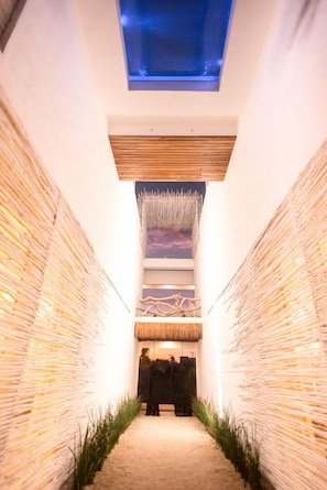 A narrow hallway with a thatched ceiling, a wooden slatted wall, and a person standing at the end. - Casa Xuul Oceanfront Villa • Chef • Staff, Pools, Hot tub & Rooftop 24 guests (Tulum)