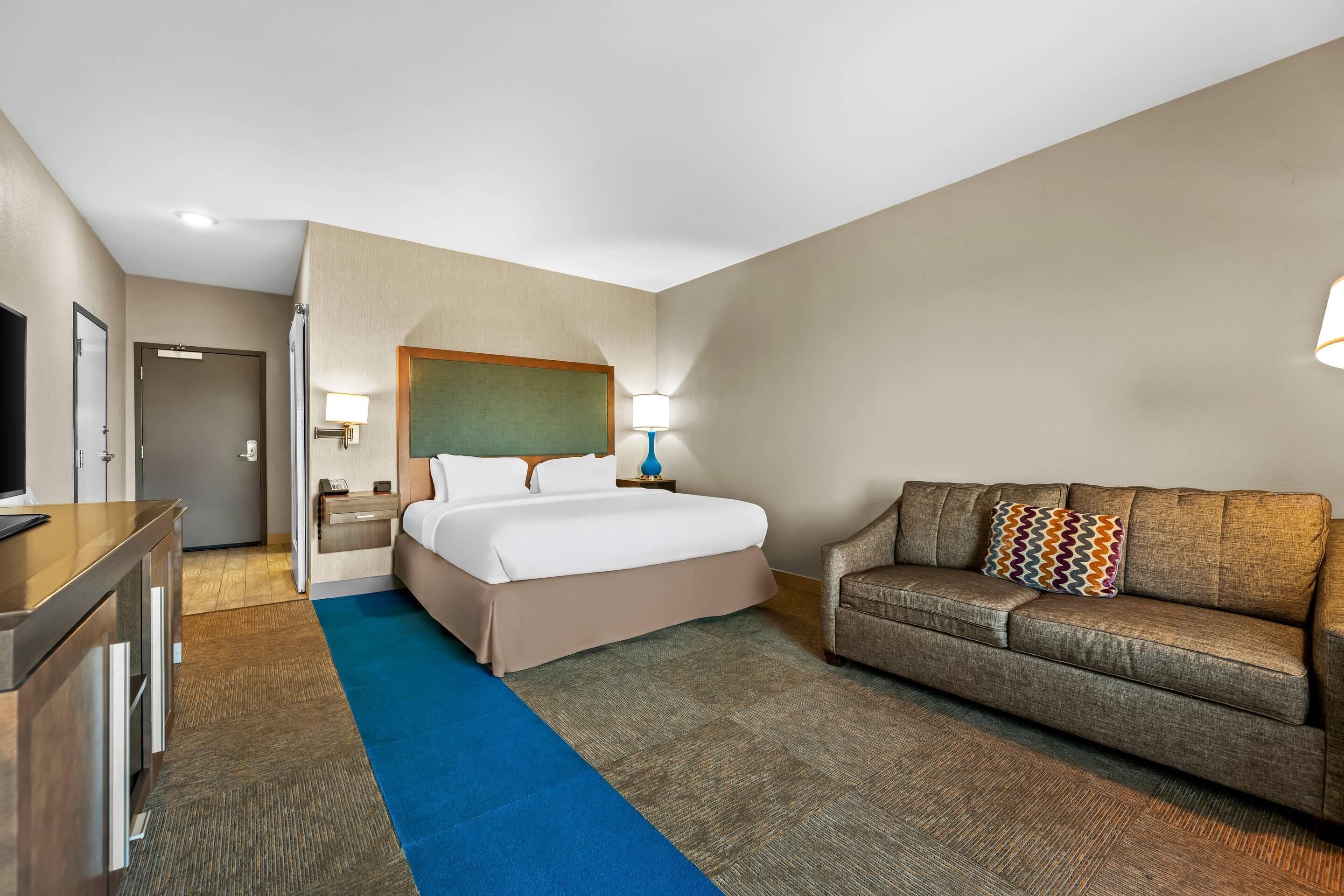 A hotel room with a bed, a sofa, a desk, and a television.