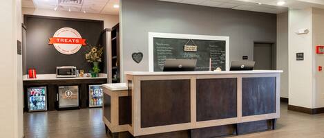 A reception desk with a chalkboard menu, a microwave, and a refrigerator.