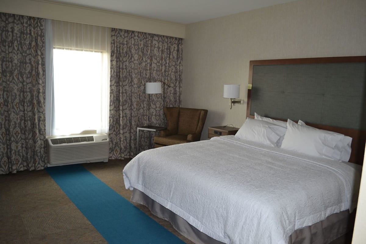 Una habitación de hotel con una cama grande, una silla, un escritorio y una ventana con cortinas.