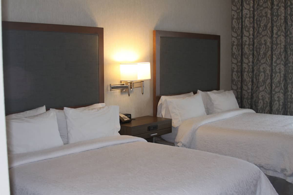 Una habitación de hotel con dos camas, una mesita de noche con lámpara y una cortina estampada.