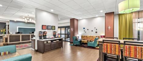 A hotel lobby with a reception desk, seating area, and a dining space.