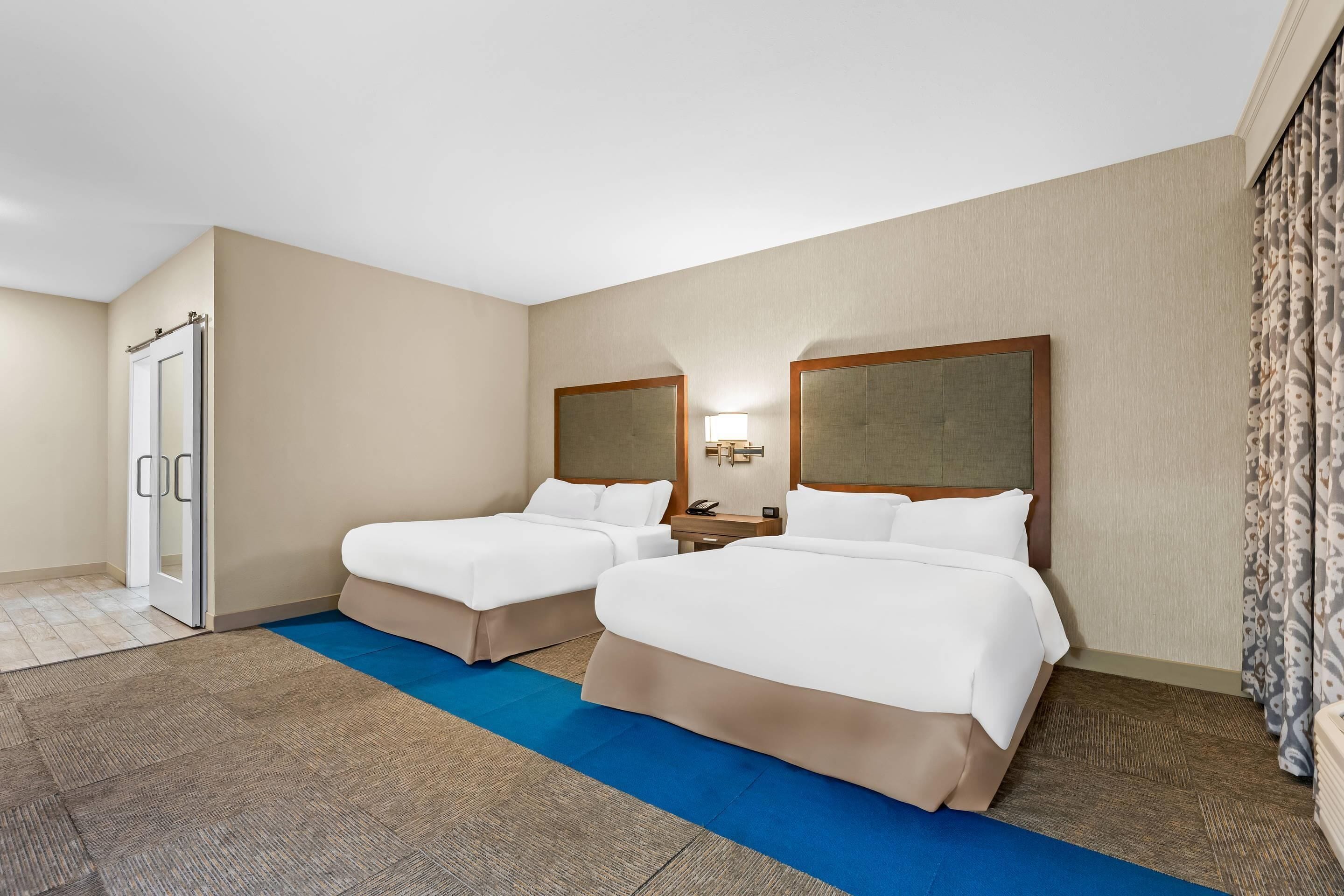Hotellihuone, jossa on kaksi sänkyä, kylpyhuone ja sininen matto.