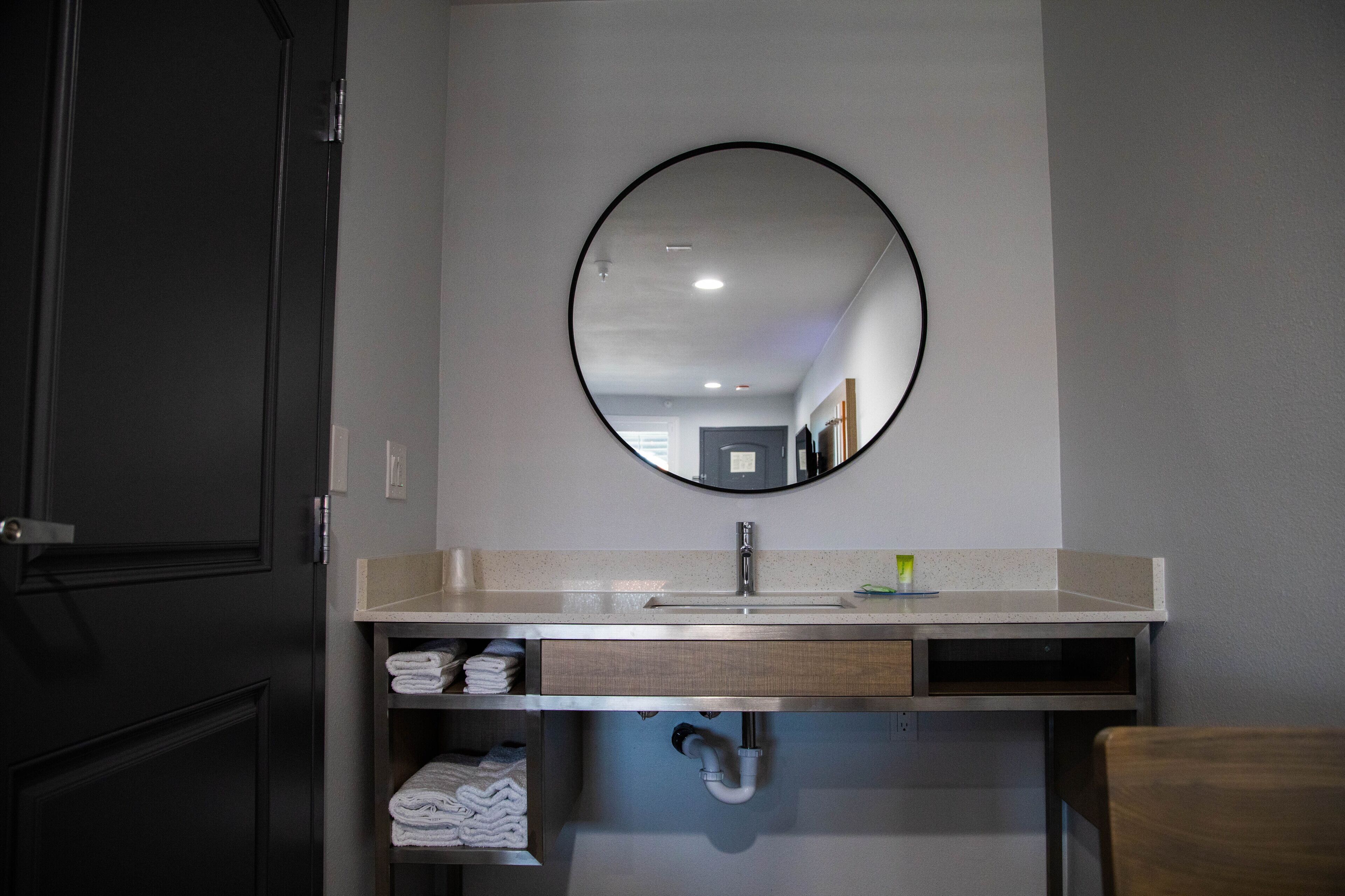 Une salle de bain avec un miroir rond, un lavabo et un porte-serviettes.