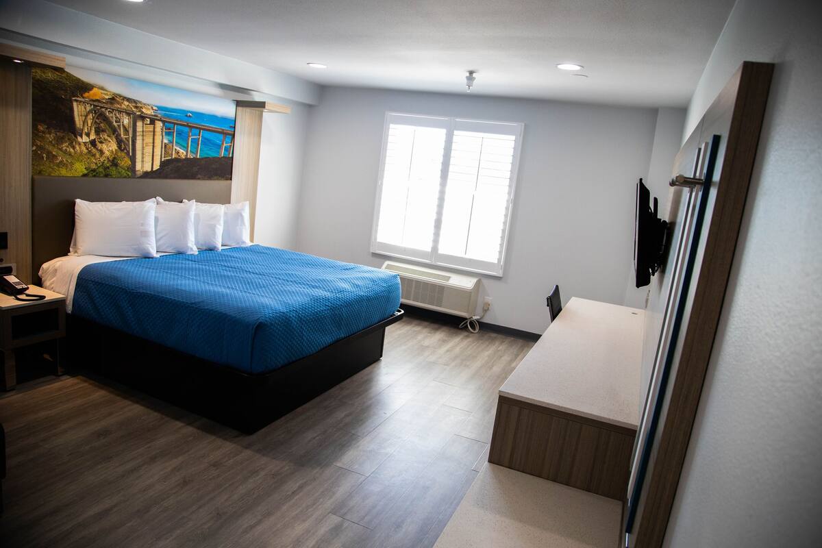 A hotel room with a bed, a desk, a window, and a mural on the wall.