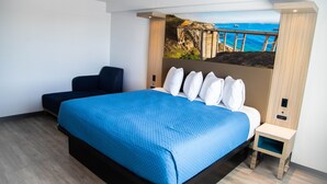 Ein modernes Hotelzimmer mit einem großen Bett, einer kleinen Couch, einem Nachttisch und einer Wandmalerei mit einer Küstenlandschaft.