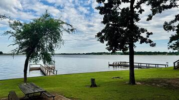 Un parque junto al lago con un muelle de madera, una mesa de picnic y zonas de césped.