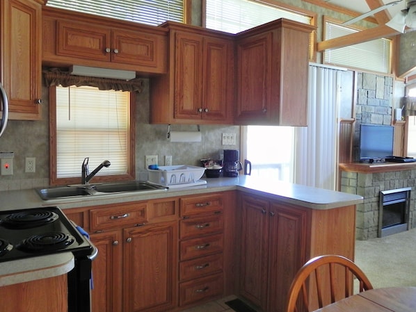 A kitchen with wooden cabinets, a stove, a sink, and a stone fireplace.