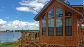 A wooden cabin with large windows, a deck, and a view of a lake. - Pope's Landing Marina (Alba)