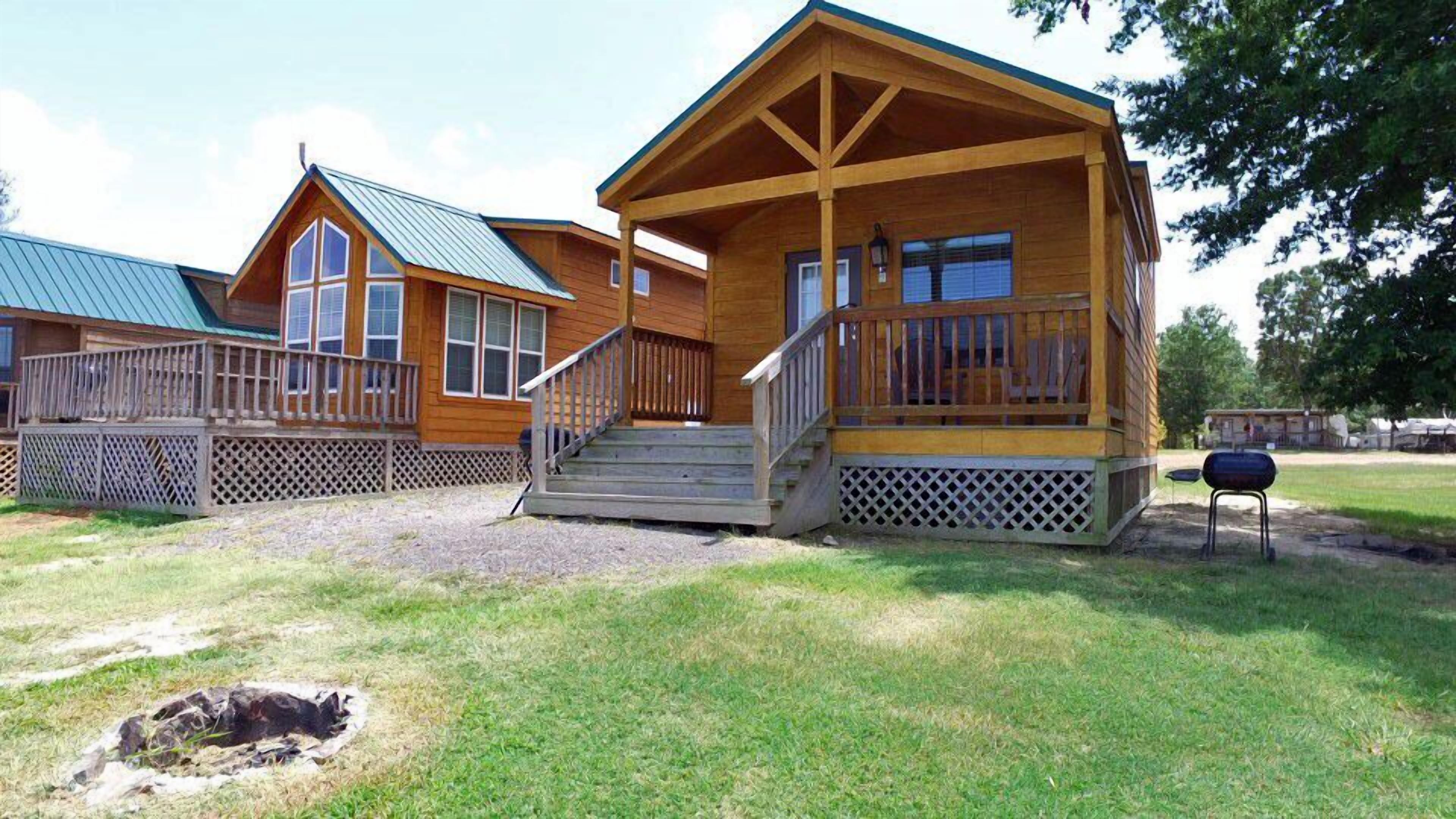 A wooden cabin with a porch and steps, a grill, and a fenced yard.