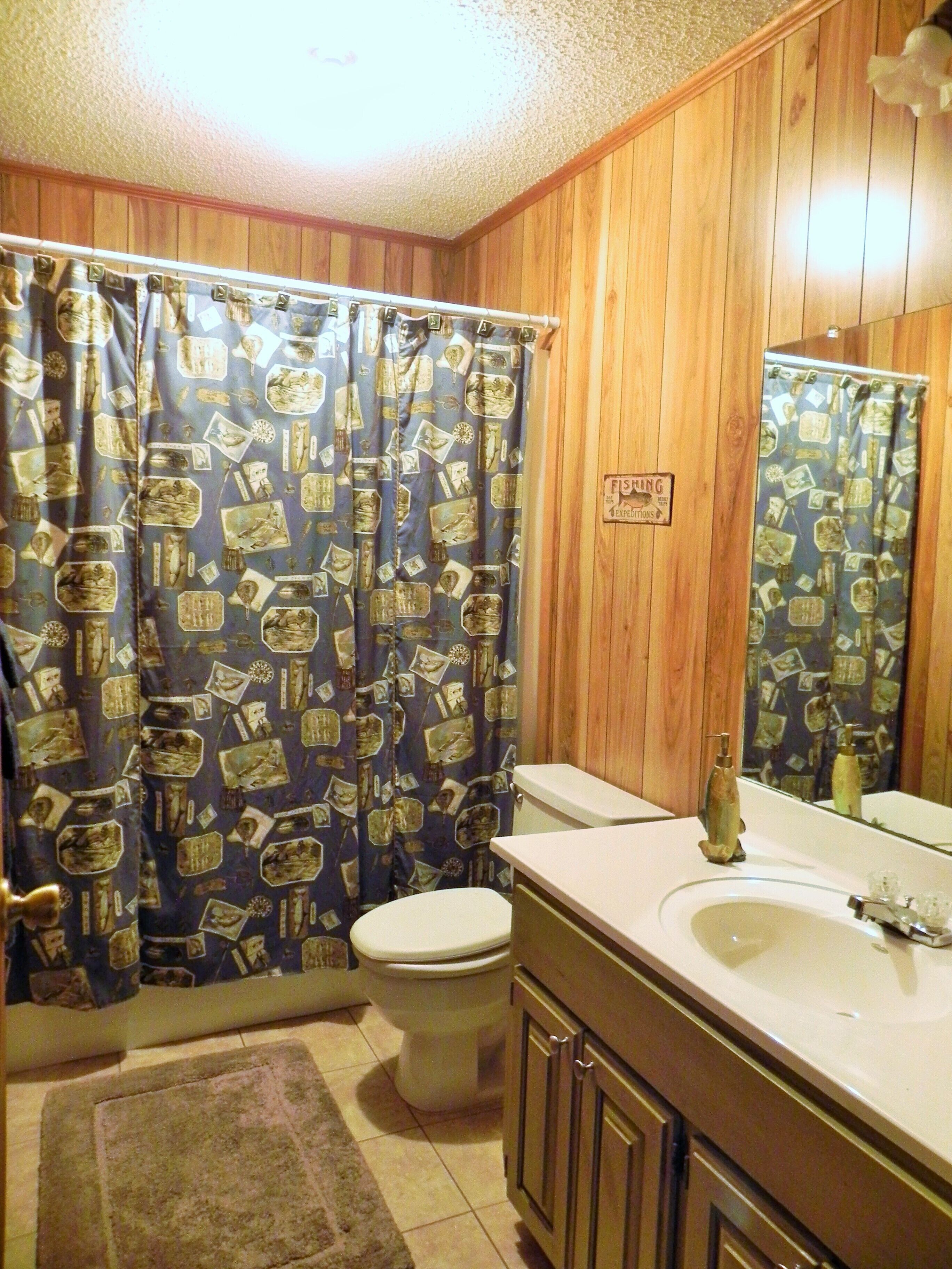 A bathroom with a wooden panel wall, a toilet, a sink, and a shower curtain with a pattern.