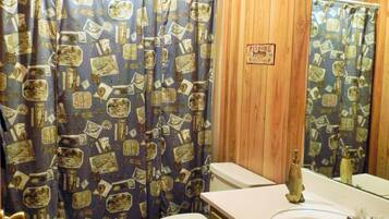 Une salle de bain avec un mur recouvert de panneaux en bois, des toilettes, un lavabo et un rideau de douche à motifs.