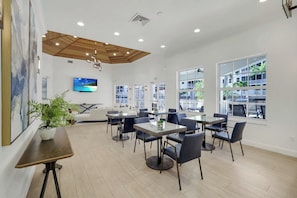 A modern hotel lobby with a wooden ceiling, large windows, a seating area with tables and chairs, and a potted plant. - Regatta - Walk to the Beach (Naples)