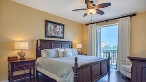 Habitación de hotel con una cama grande, dos mesitas de noche con lámparas, un ventilador de techo, una ventana con cortinas y vistas a edificios.