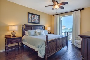 A hotel room with a large bed, two bedside tables with lamps, a ceiling fan, a window with curtains, and a view of buildings.