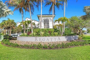 A sign with 'REGATTA' in front of a building with a white facade and a central tower, surrounded by palm trees and greenery.