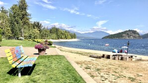 A bench with colorful artwork, a grassy area, a wooden dock, and a lake with boats.