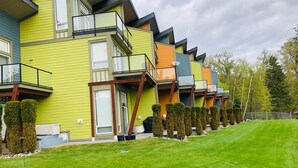 A row of modern multi-story buildings with balconies, a well-maintained lawn, and neatly trimmed hedges.