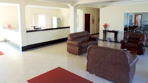 A spacious living area with a reception desk, two sofas, a dining table, and a red rug. - Hotel Pequeno Mundo II (Campo Verde)
