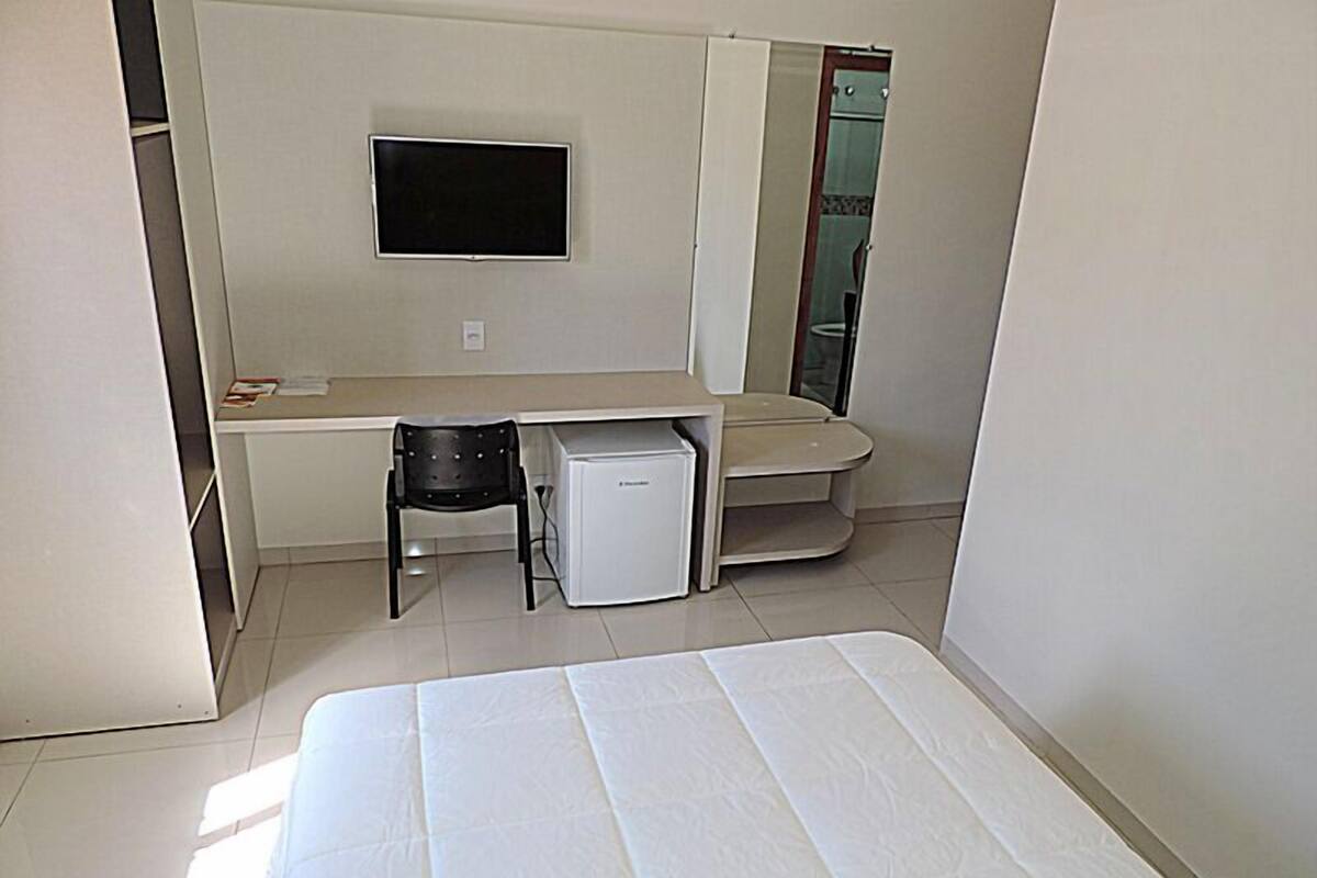 A compact room with a bed, a small desk, a chair, and a television mounted on the wall.