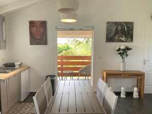 A modern kitchen with a wooden countertop, a dining table with chairs, and a view of a lush garden through a sliding door. - Loft Paradis hhhhhhh (Sainte-Anne)