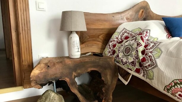 Ein Bett mit einem hölzernen Kopfteil, das einen geschnitzten Tierkopf zeigt, einer Lampe und einem Bettsofa mit Muster.