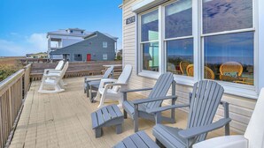Een houten terras met Adirondack-stoelen en uitzicht op de oceaan.