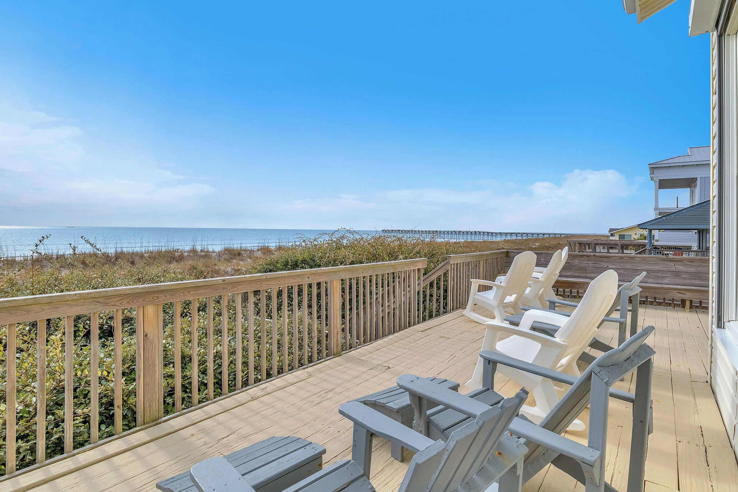 A wooden deck with chairs and tables overlooking a beach and a pier.