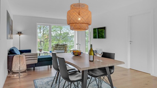 A modern dining area with a wooden table, black chairs, a woven pendant light, and a bowl of fruit on the table. - Nice apartment in Hornbæk with WiFi (Hornbæk)