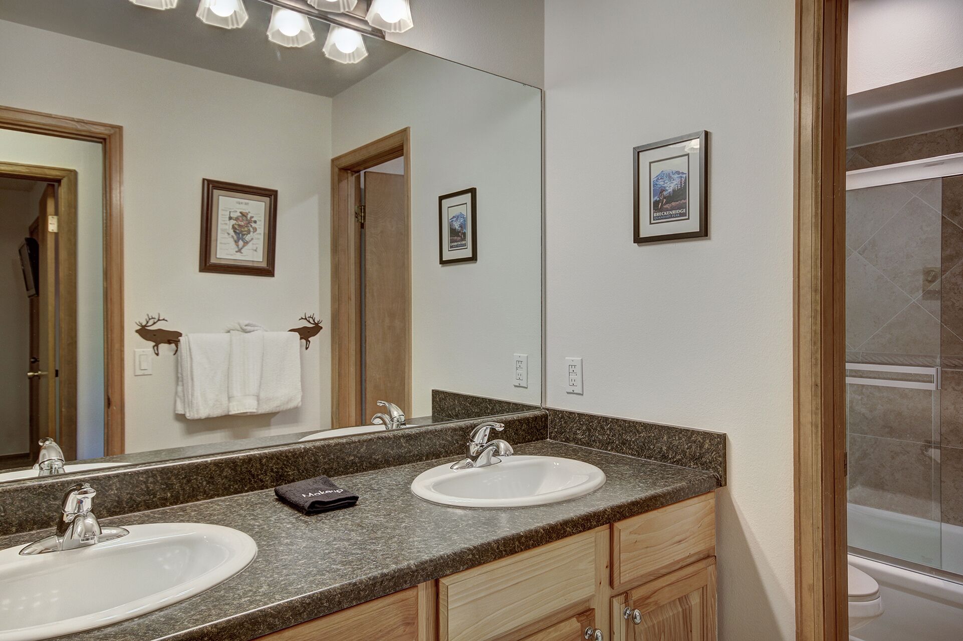 Une salle de bain avec deux lavabos, un grand miroir et des tableaux encadrés accrochés au mur.