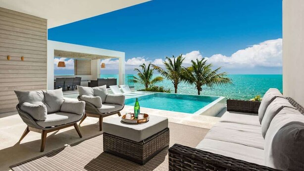 Un espace de détente extérieur moderne, doté d’une piscine, de mobilier blanc et offrant une vue dégagée sur l’océan.
