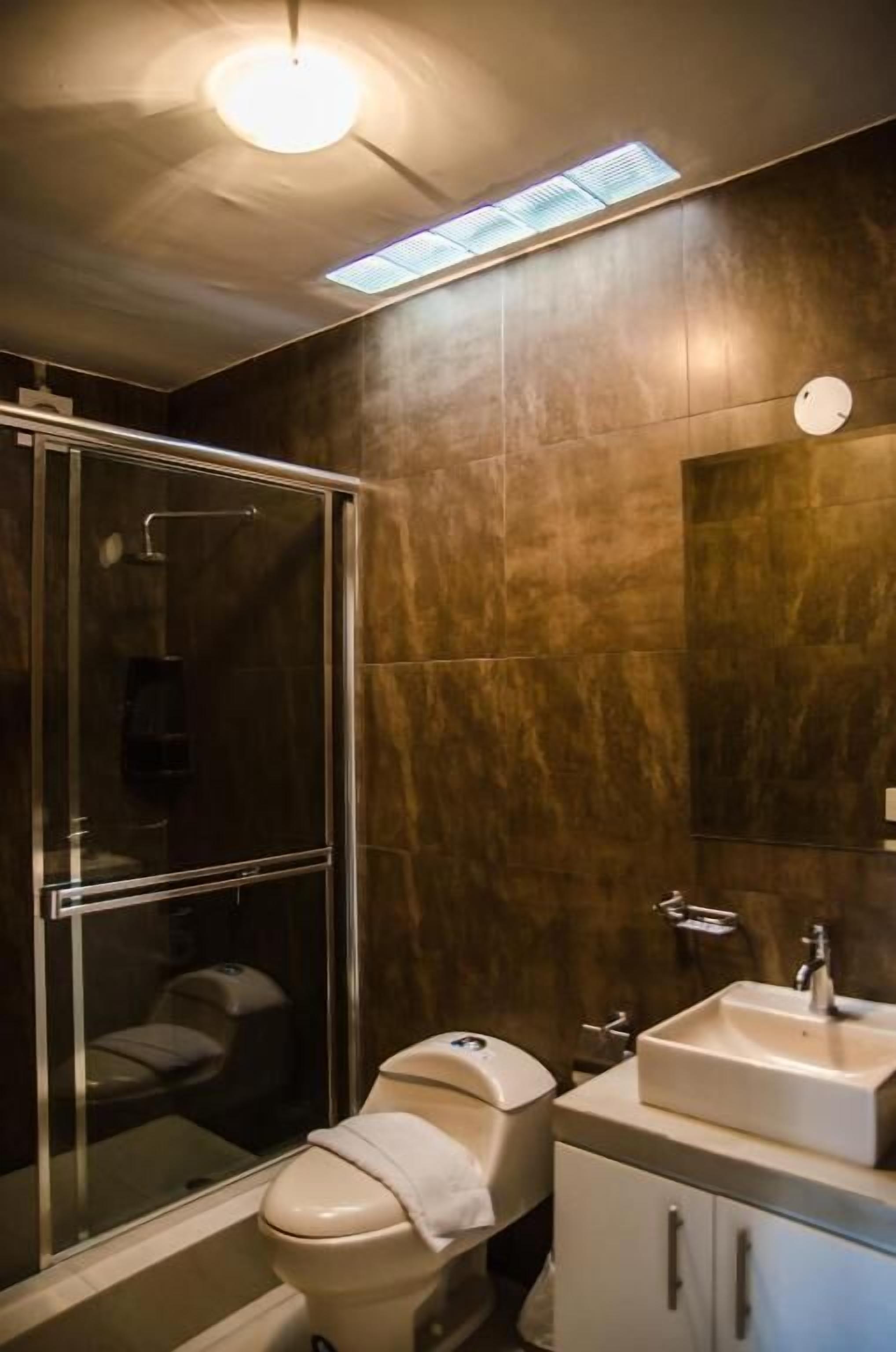 A modern bathroom with a glass-enclosed shower, a toilet, and a sink with a mirror above it.