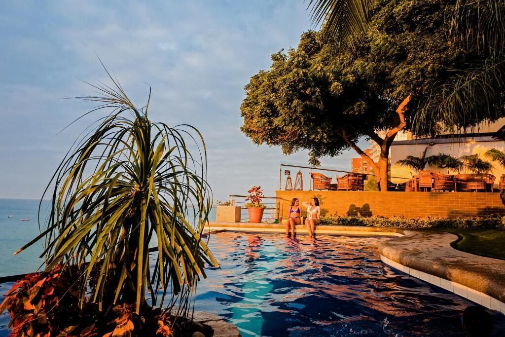 Un espace piscine avec vue sur la mer, entouré de palmiers et de chaises longues.