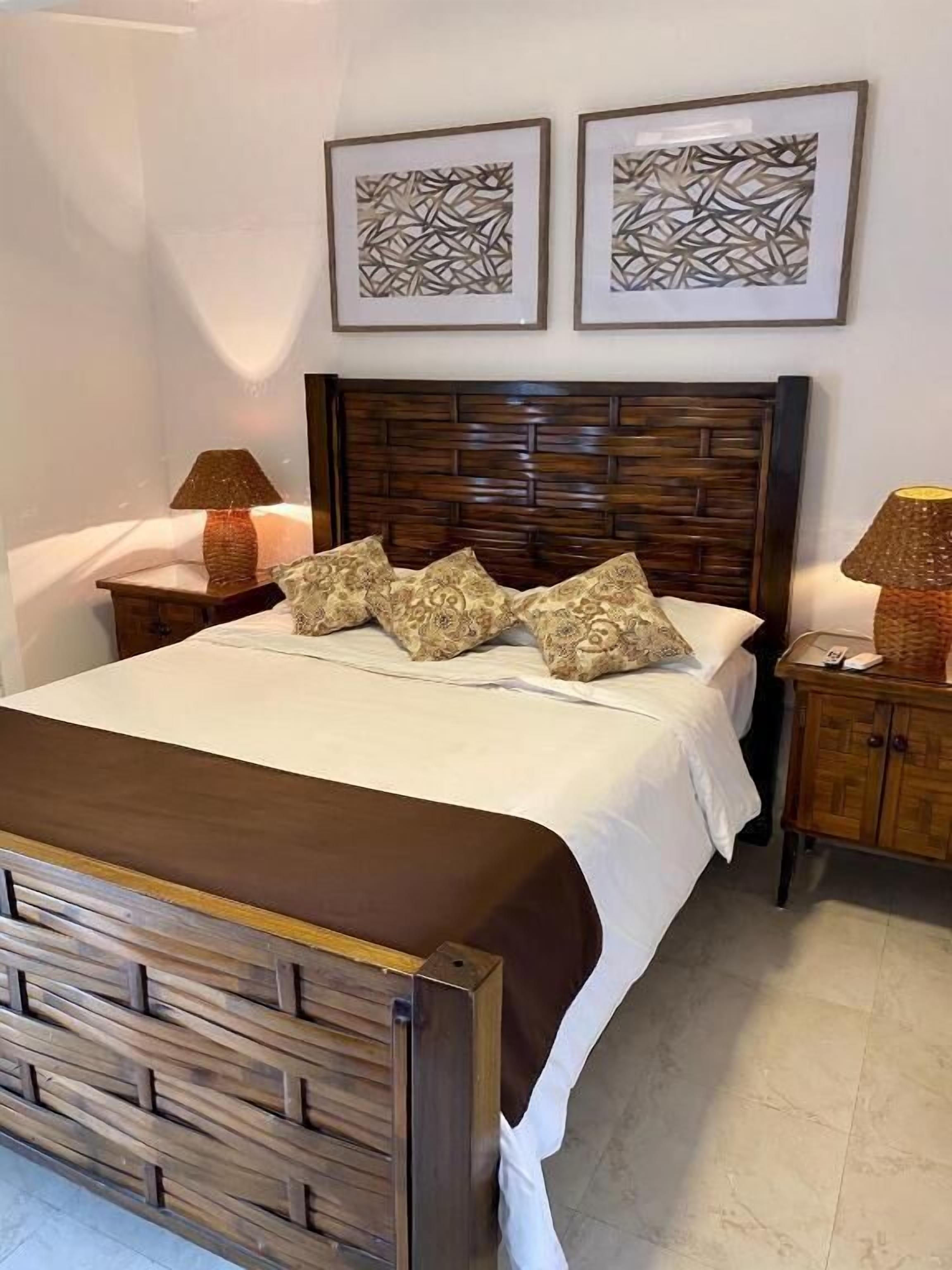 Un lit bien fait, avec une tête de lit en bois, deux tables de chevet avec des lampes et deux œuvres d’art abstraites accrochées au mur.
