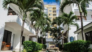 Un patio con palmeras, fuente de agua y un edificio con balcones.