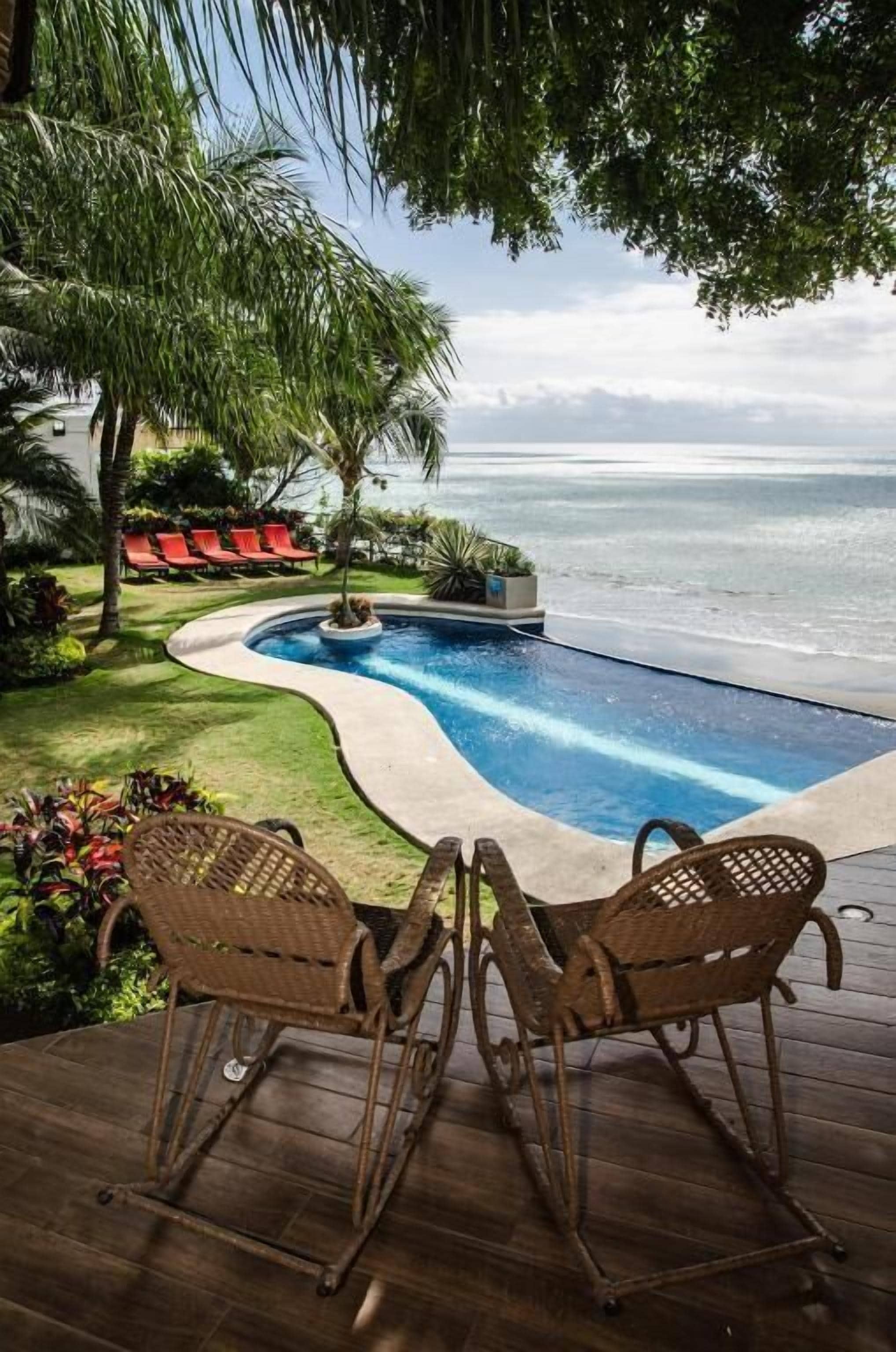 Ein Pool mit Blick auf das Meer, umgeben von roten Liegestühlen und einer Holzterrasse.