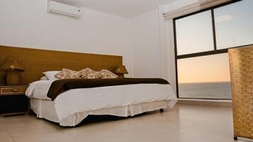 A bedroom with a large window, a bed with white bedding, a nightstand with a lamp, and a woven headboard.