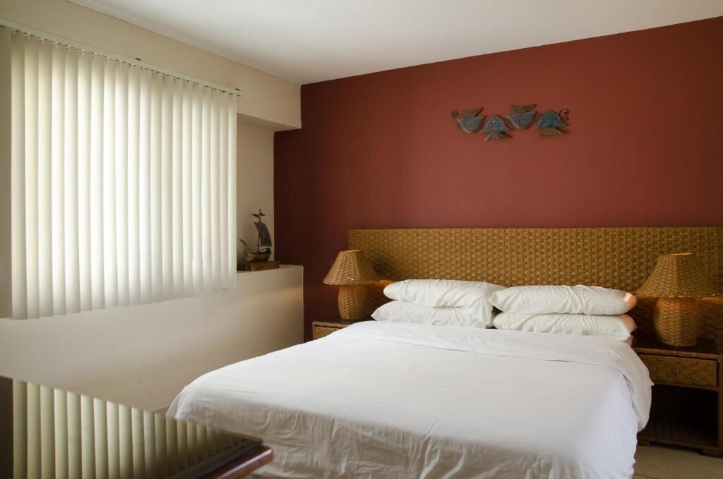 A hotel room with a large bed, a headboard with a patterned design, two bedside lamps, and a wall-mounted decoration.