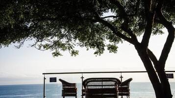 A bench area with a view of the sea, a tree, and a glass railing.