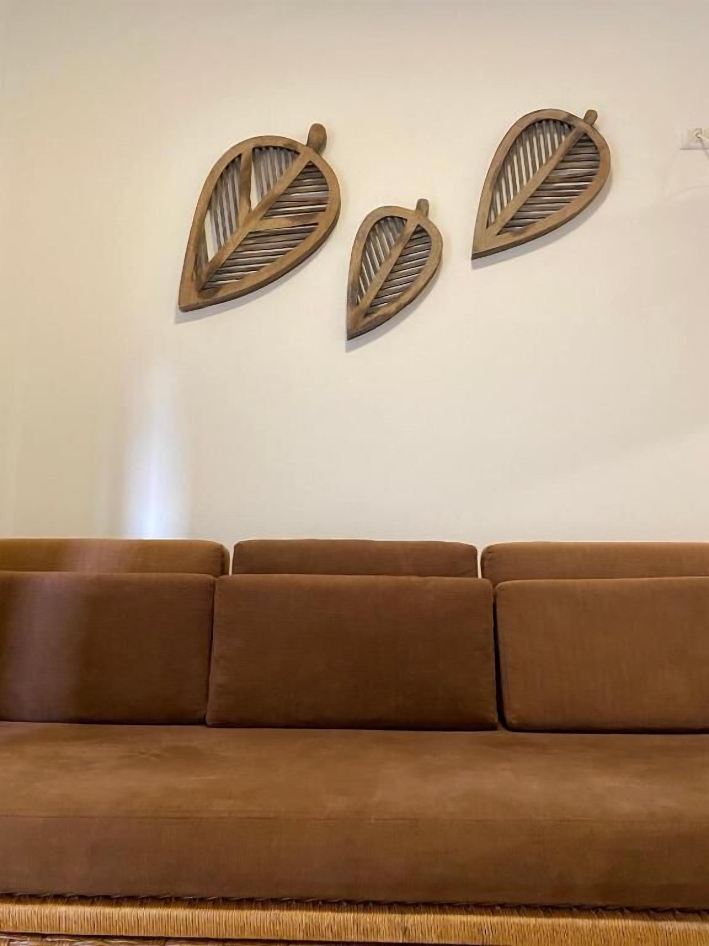 Un canapé marron est placé contre un mur uni, et deux éléments décoratifs en bois, en forme de feuilles, ornent ce mur.