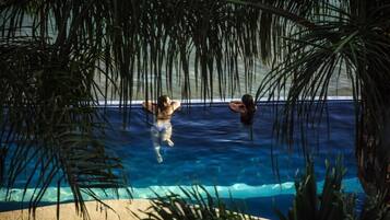 A swimming pool with two people in the water, surrounded by palm trees.