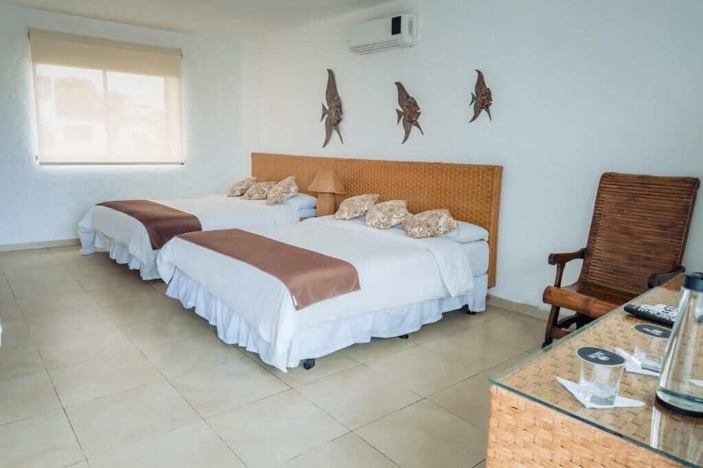 A hotel room with two beds, a wooden headboard, a desk with a glass top, and decorative wall art.