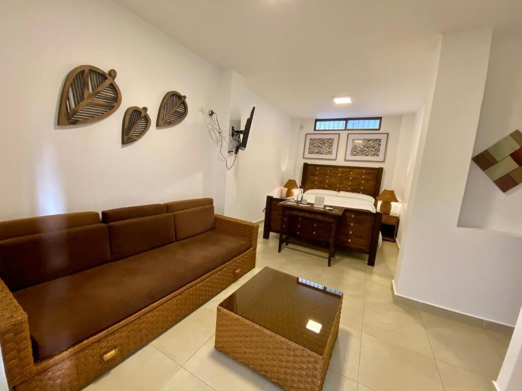 Una sala moderna con un sofá marrón, una mesa de centro de vidrio, un escritorio de madera y una cama con cabecero de madera.