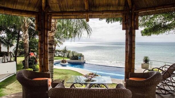 Un espacio al aire libre cubierto con mobiliario de mimbre, una piscina y vistas al océano.