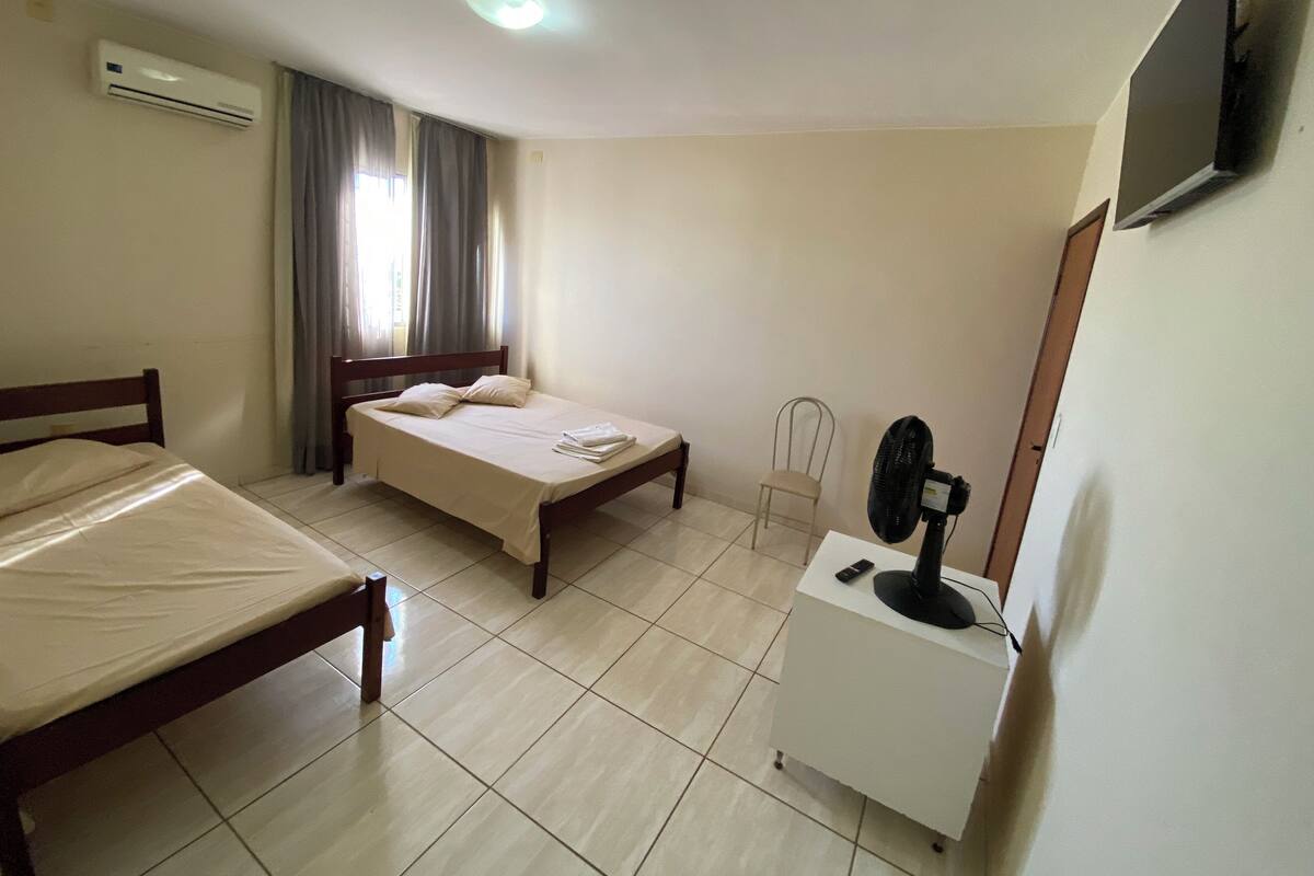 A hotel room with a bed, a chair, a desk with a fan, and a TV on the wall.